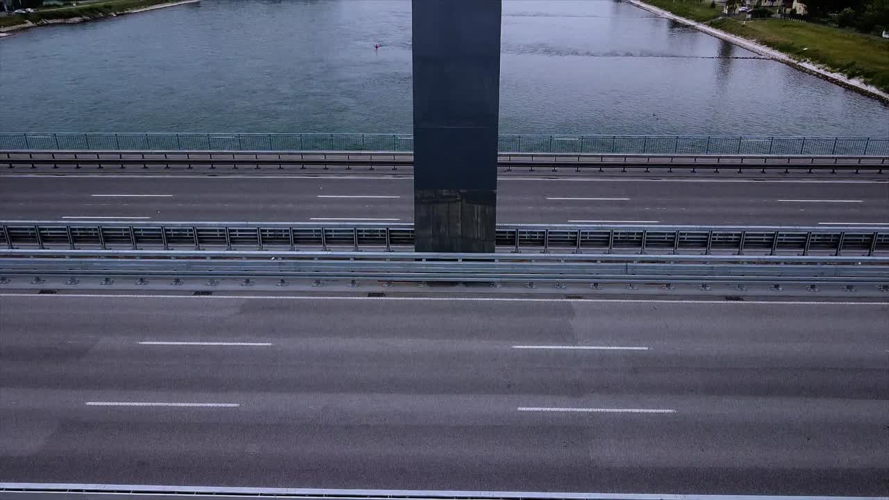Drone footage with a fixed position while camera shifts up vertically next to a beautiful bridge with cars and background river view in Europe