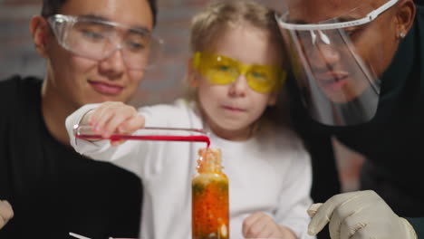 girl licks lips and pours red paint into flask near teachers