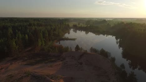 Misty-morning-sunlight-over-autumn-forest-lake-and-scenic-countryside-landscape-aerial-wide-view