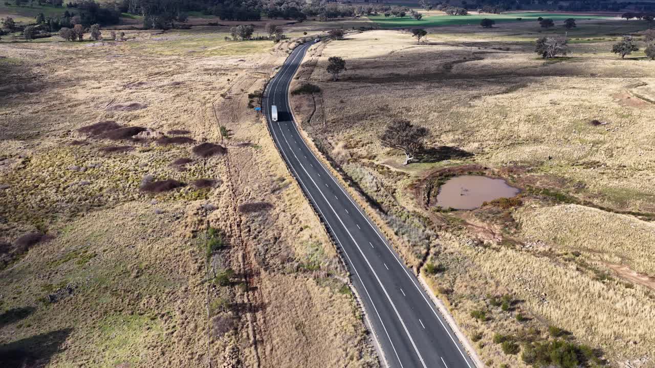 Aerial footage tracks a winding rural road through dry grasslands and scattered trees under natural daylight, with smooth forward drone movement and clear visibility