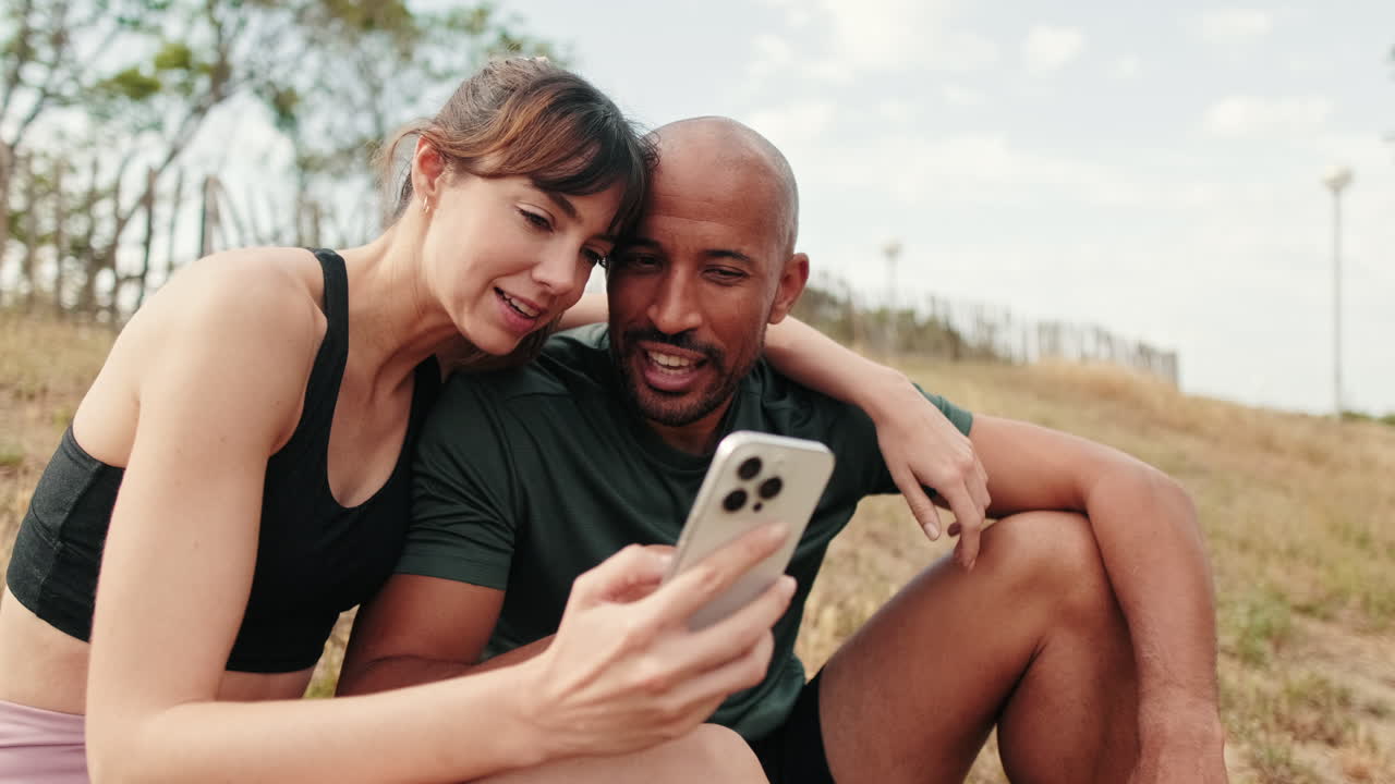 Happy Couple Sitting Outdoors and Looking at Smartphone