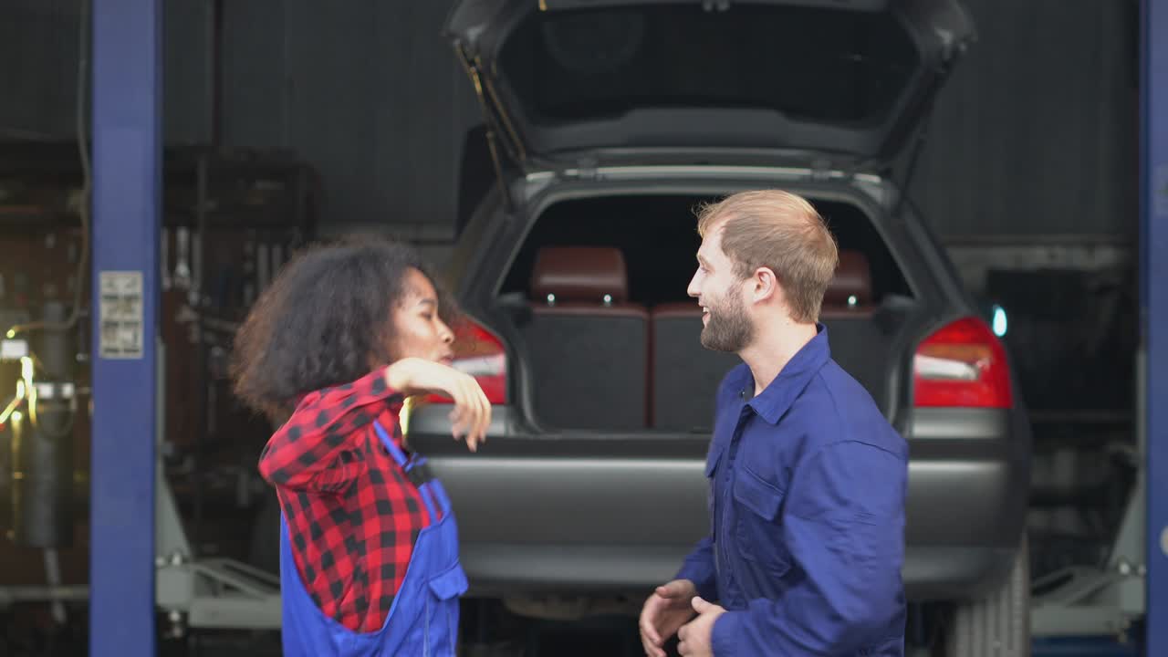 una mujer y un mecánico bailando en medio del garaje.