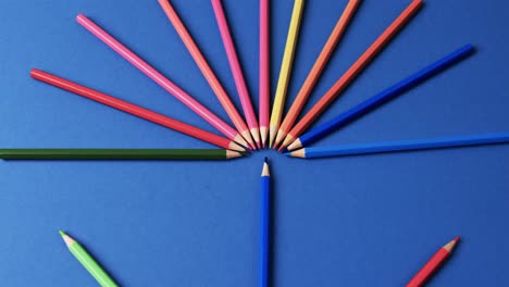Close-up-of-crayons-arranged-on-blue-background,-in-slow-motion