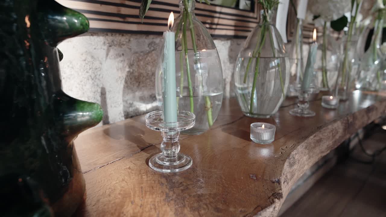 burning candles and glass vases with stems on wooden table with natural texture