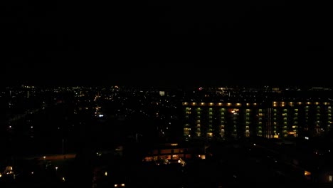 Drone-Ascending-On-The-Cityscape-At-Night-With-Exploding-Fireworks-In-Distance