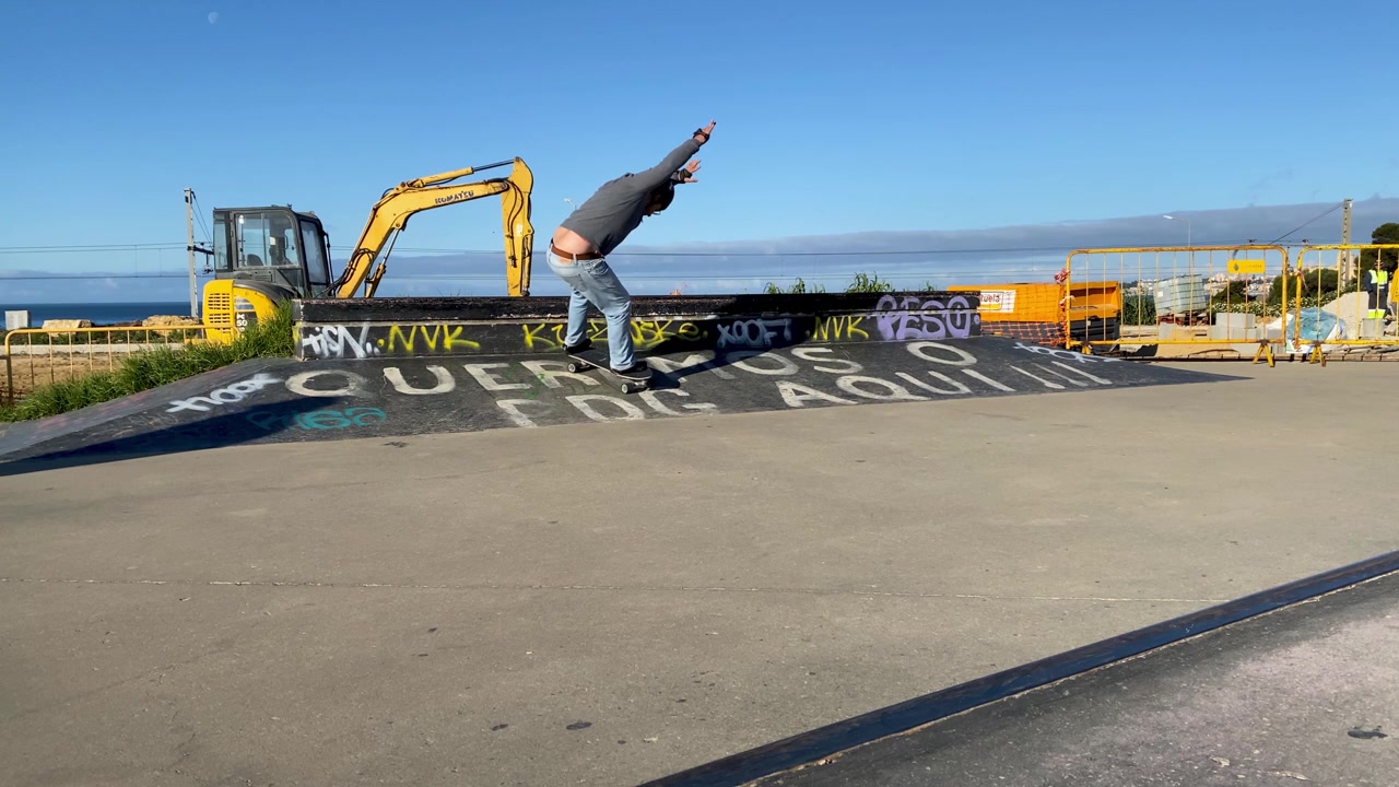 Inquadratura fissa di un uomo che attraversa le strutture di uno skatepark con graffiti, indossando equipaggiamento di sicurezza.