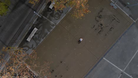 Luftaufnahme-Von-Oben-Nach-Unten-Einer-Person,-Die-Bei-Sonnenuntergang-In-Deutschland-Auf-Einem-Städtischen-Basketballplatz-Liegt