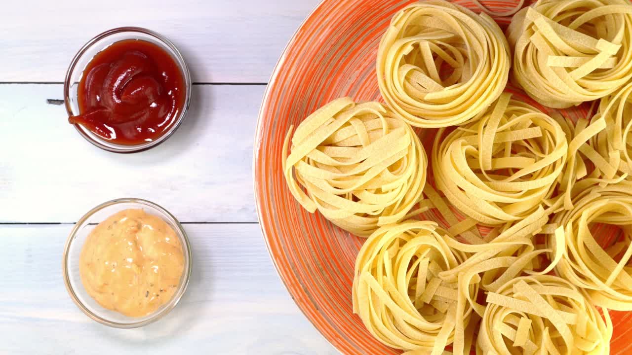 요리되지 않은 원시 이탈리아 태글라텔레 파스타가 접시에서 회전 테이블에서 천천히 회전합니다.