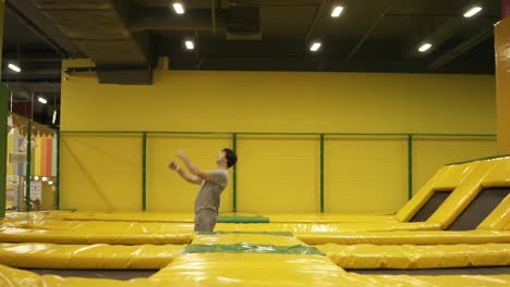 young male athlete in beige t-shirt and shorts hopping on trampoline with somersault and body twist picking.