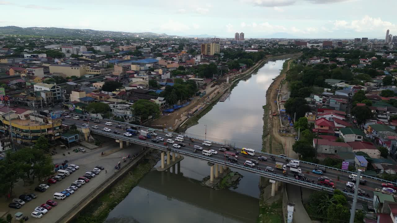 Medium drone approach to bridge crossing Marikina River cutting through dense urban area in Metro Manila at daylight, evening traffic commute