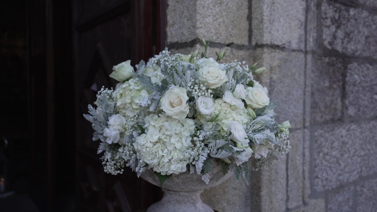 Stor hvid blomsteropsats udstillet i en udsmykket vase uden for en stenkirke.