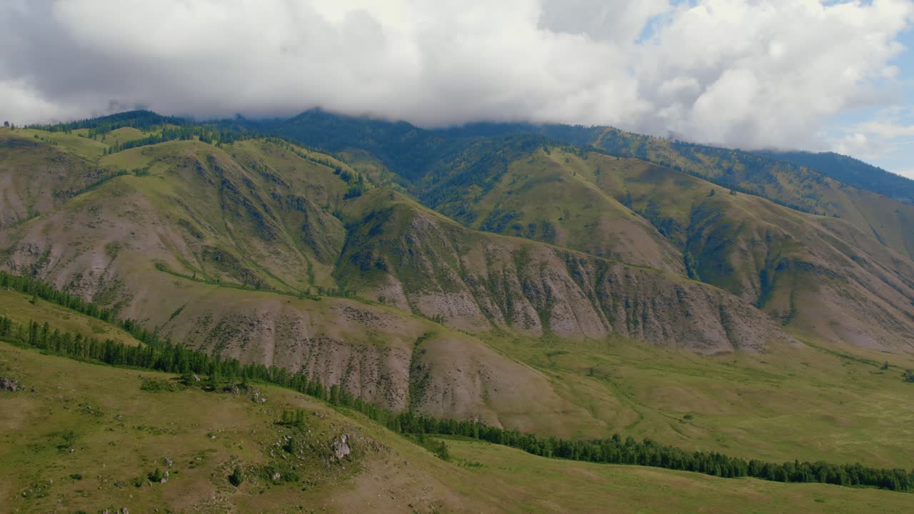 Ampia ripresa aerea di colline verdi e aspri pendii montuosi nella valle di Ak-Kem, Repubblica dell'Altai, Russia, con nuvole spettacolari e uno scenario di natura selvaggia e remota.