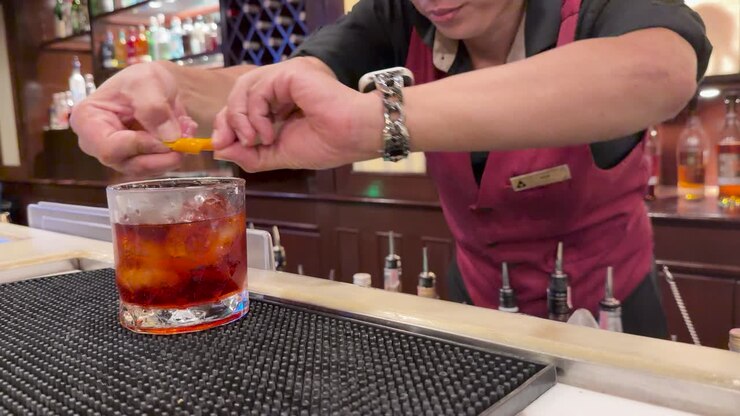 Un barista aggiunge una scorza d'arancia a un cocktail Negroni in un bar elegante, con una calda illuminazione ambientale