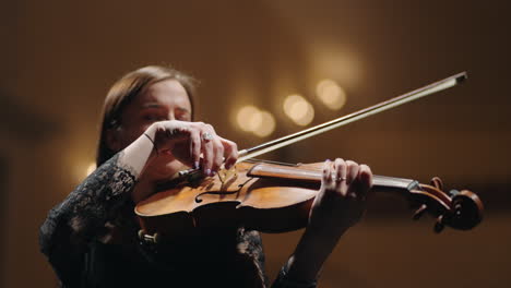 brunette lady in black is playing fiddle in philharmonic hall female musician in symphonic orchestra