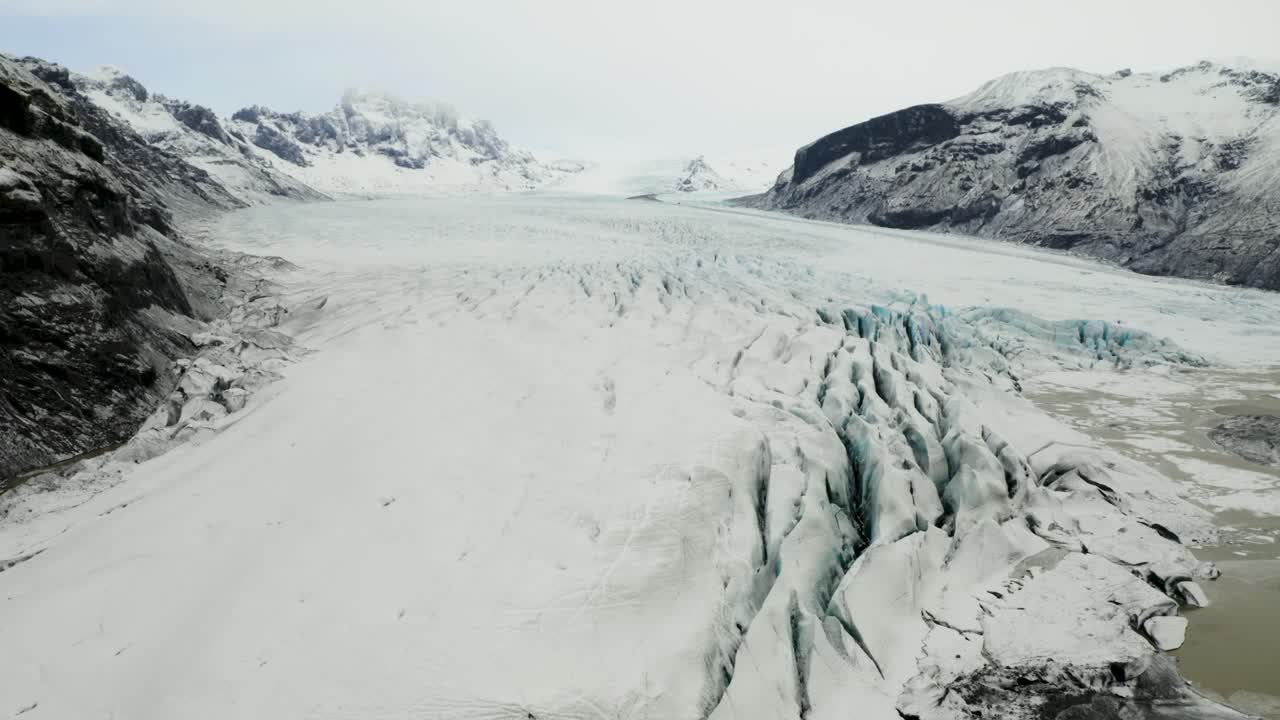Sweeping drone shot showcasing the vast icy surface of Svinafellsjokull glacier, its deep crevasses, and the adjacent meltwater lagoon.