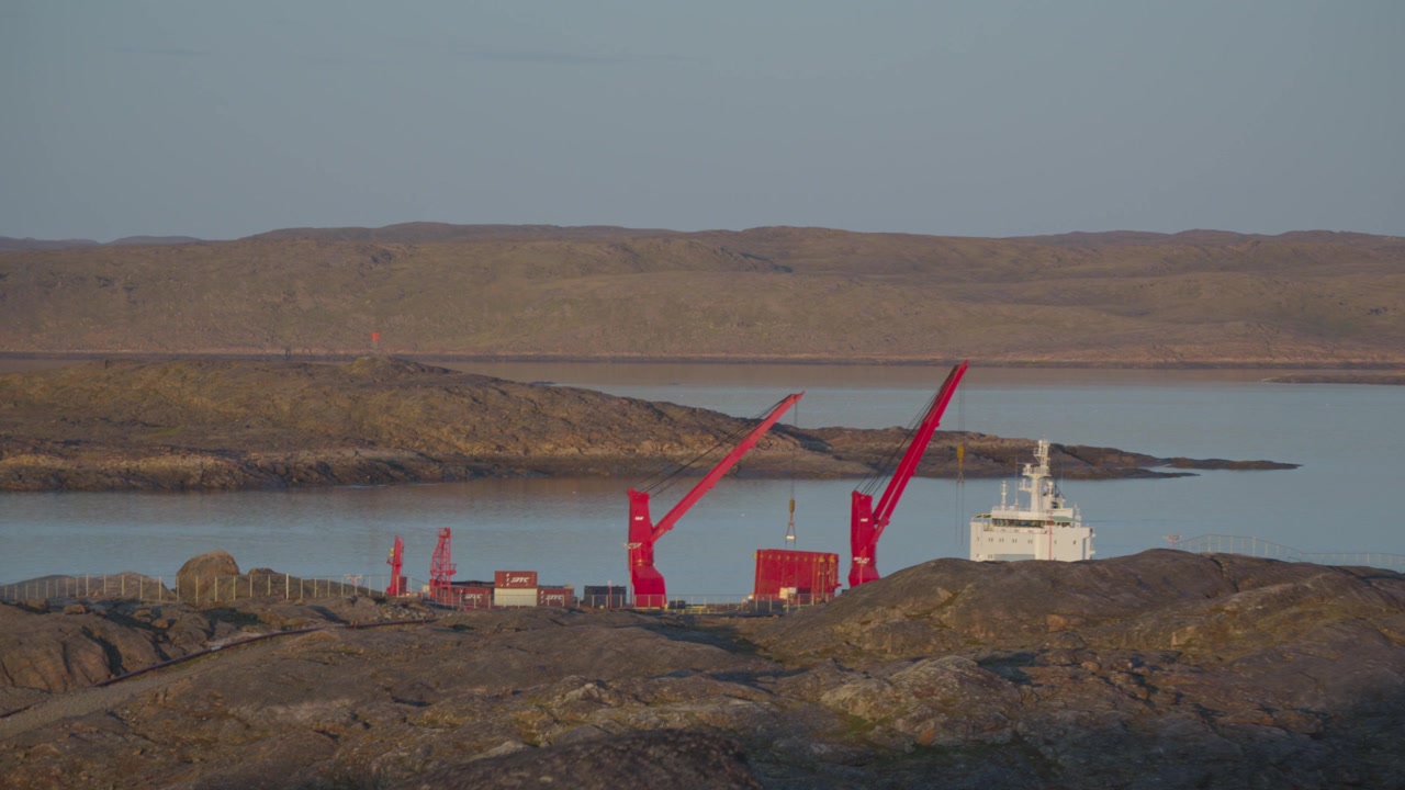 Toma con teleobjetivo capturando grúas de cubierta pesadas montadas directamente en un buque de carga de transporte marítimo descargando contenedores en la instalación del Puerto de Aguas Profundas de Iqaluit