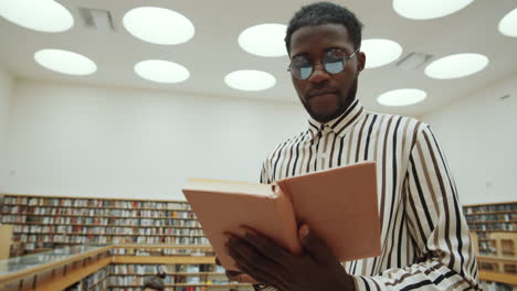 afro man standing in library and reading book