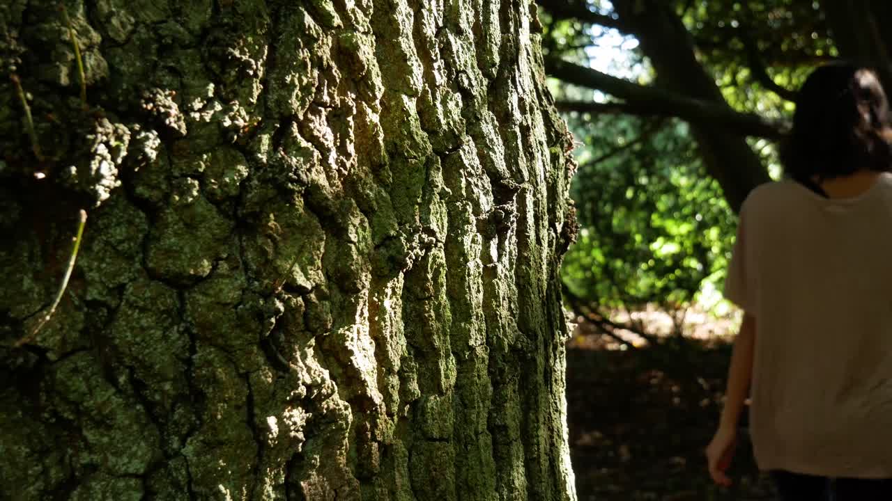 mujer con uñas rojas pone su mano en un árbol al pasar