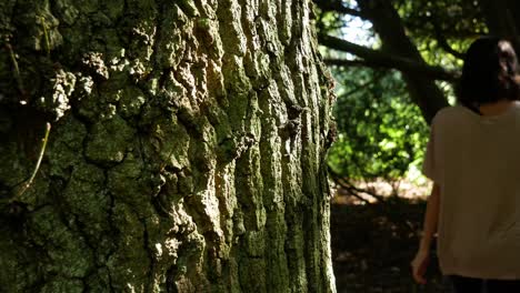 woman with red nails puts her hand on a tree as she passes