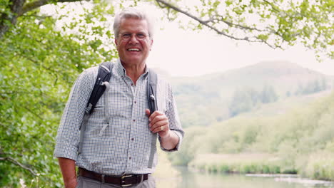 slow motion portrait of smiling senior man hiking along path by river in uk lake district