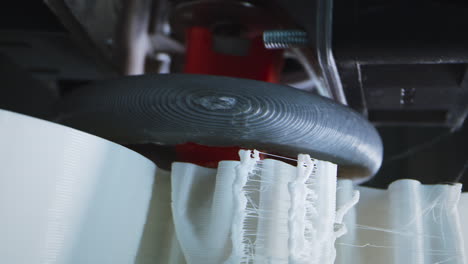 close-up of a 3d printer in action, showing the nozzle printing a white object with visible stringing