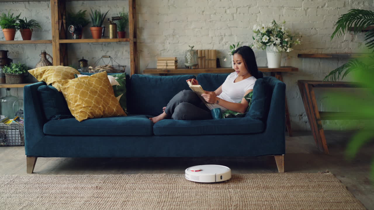 Woman Reading on a Sofa with Robotic Vacuum