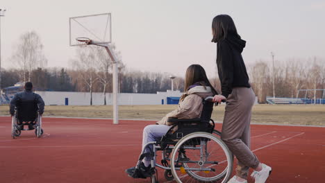 mujer discapacitada en silla de ruedas y su amiga mirando a sus amigos jugando al baloncesto 2