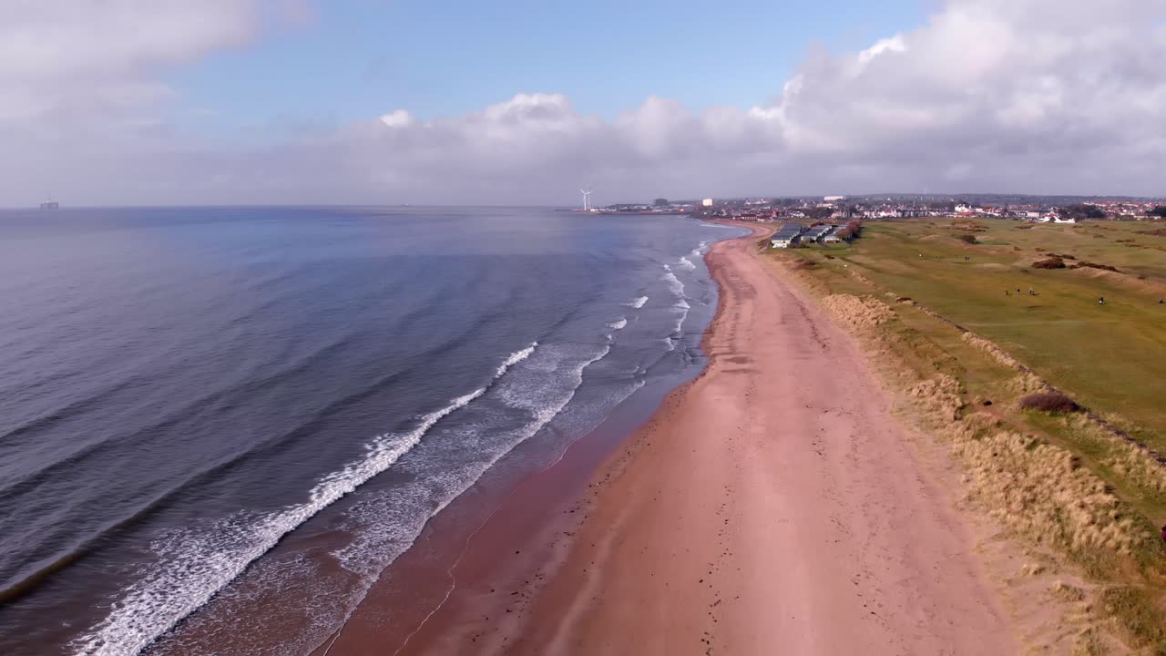 vista aérea del campo de golf scottish links junto a arenas doradas y suaves olas rompiendo en la playa