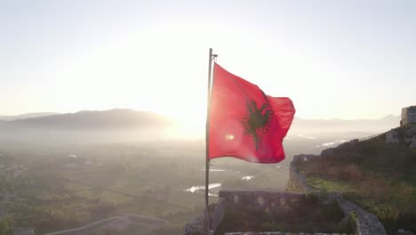 Close-up-shot-of-albanian-flag-on-top-of-Schloss-Shkodra-during-sunrise,-aerial