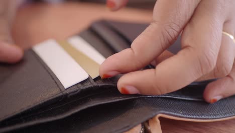 close up of a woman's hands reaching into a wallet and grabbing a credit card