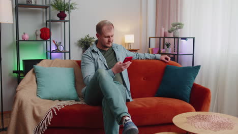 cheerful young man sitting on sofa, using mobile phone share messages on social media application