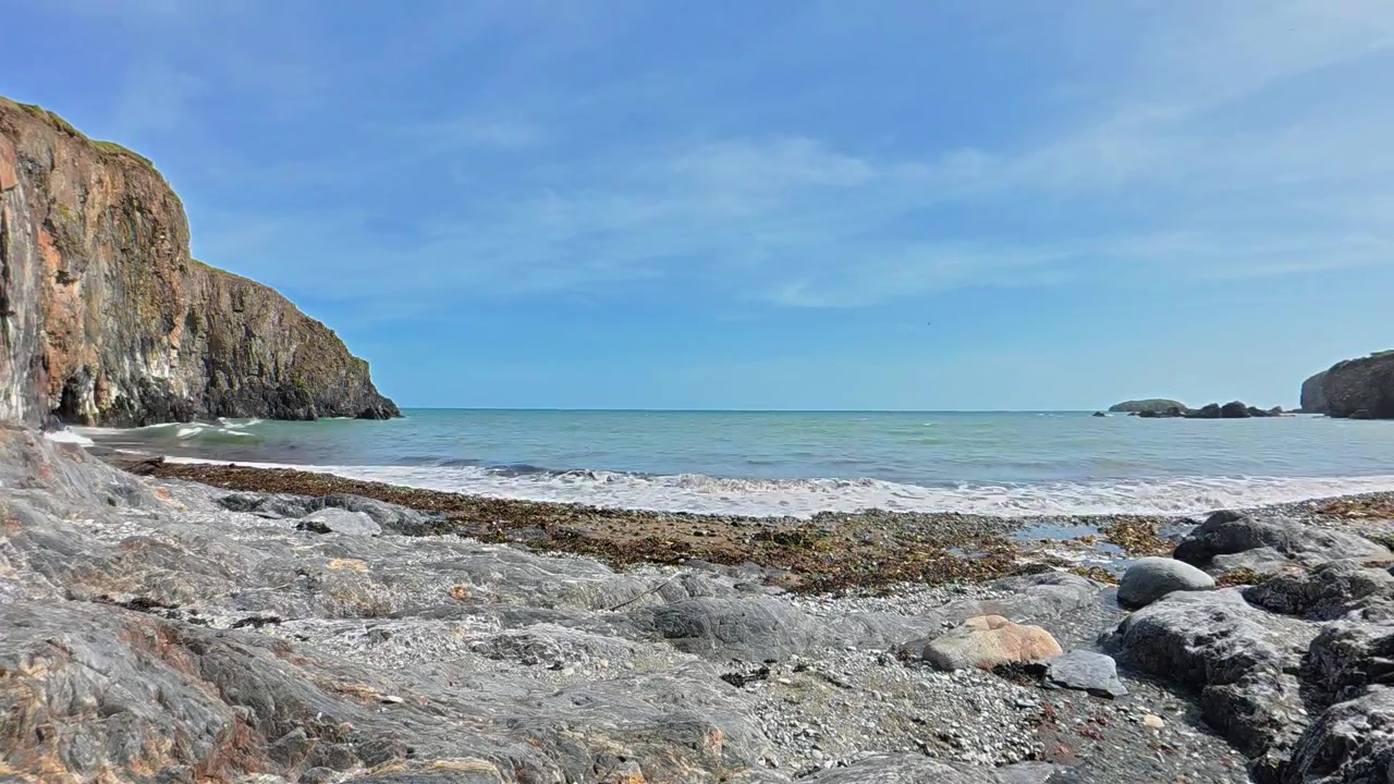 愛爾蘭沃特福德銅海岸的岩石海灘縮時攝影，輕柔海浪拍打著，藍天下的夏日風光。