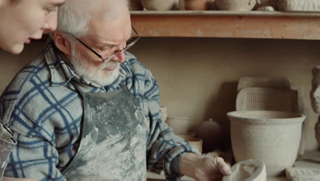 elderly potter working with assistant in workshop