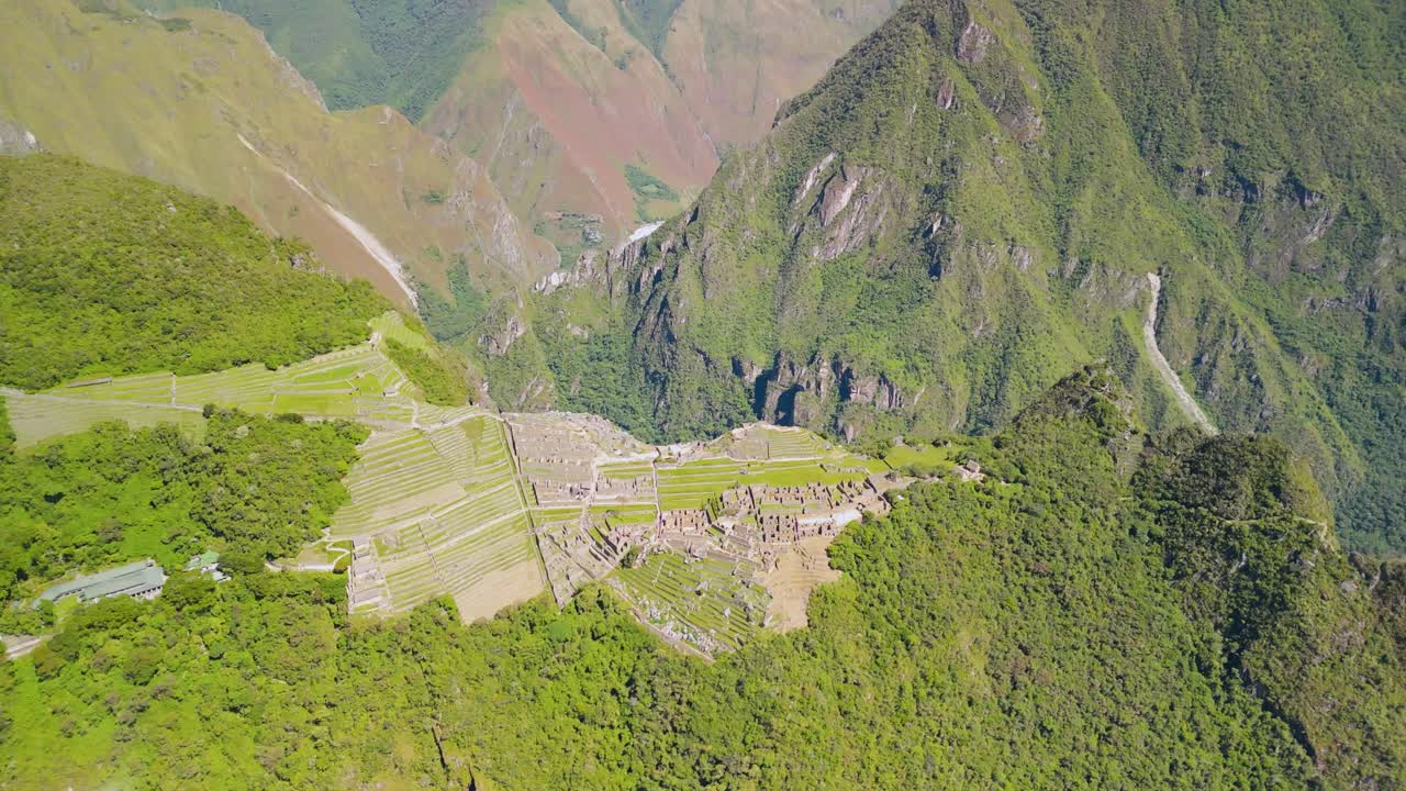 Wide drone establishing pullback of Machu Picchu plateau with terraced stone walls and steep surrounding peaks