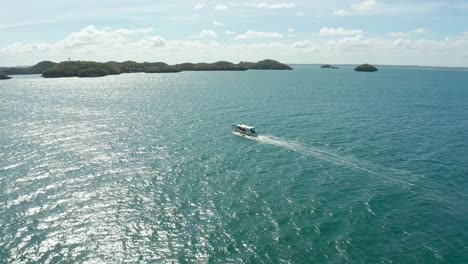 Persecución-Aérea-En-ángulo-De-Un-Barco-Banca-Navegando-En-Aguas-Azules-Hacia-Islas-4k