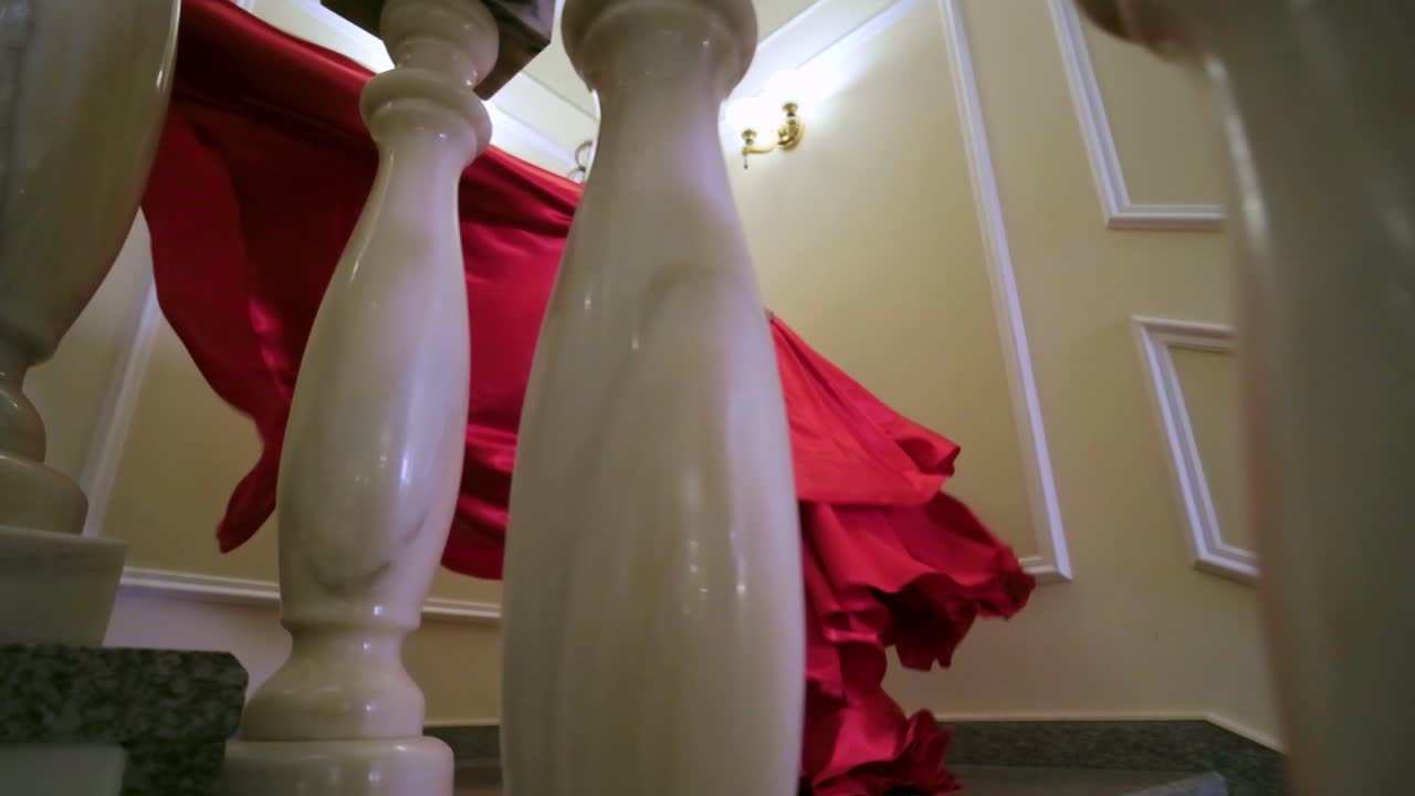 A Mysterious Figure in a Flowing Red Dress Gracefully Navigates Down a Staircase, Captivating the Atmosphere with Elegance and Intrigue