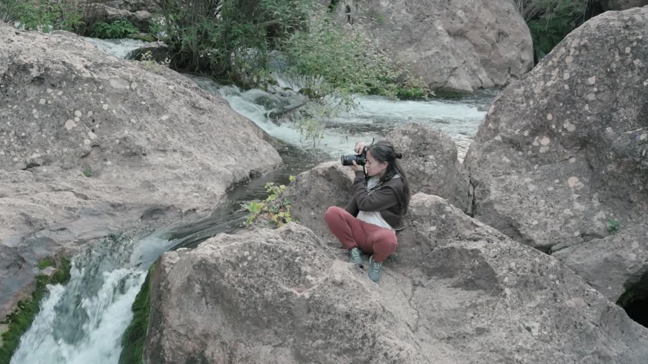 Brunette woman photographing nature, surrounded by rocks and plant life, near a waterfall on the Mundo River in Albacete
