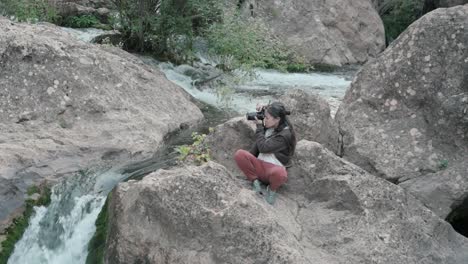 brunette woman photographing nature, surrounded by rocks and plant life, near a waterfall on the mundo river in albacete