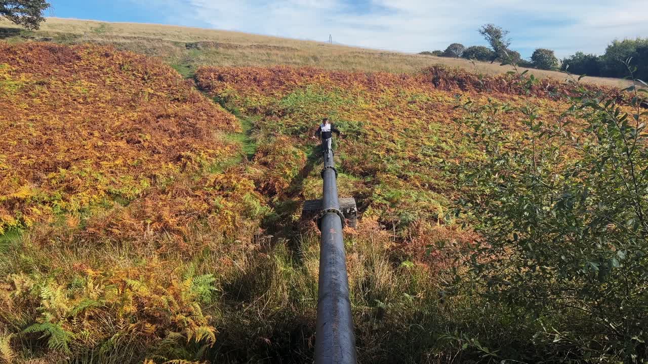 niño jugando en una tubería de agua en una escena campestre boscosa con helechos dorados de otoño y el resplandor de la luz del sol que entra desde la izquierda