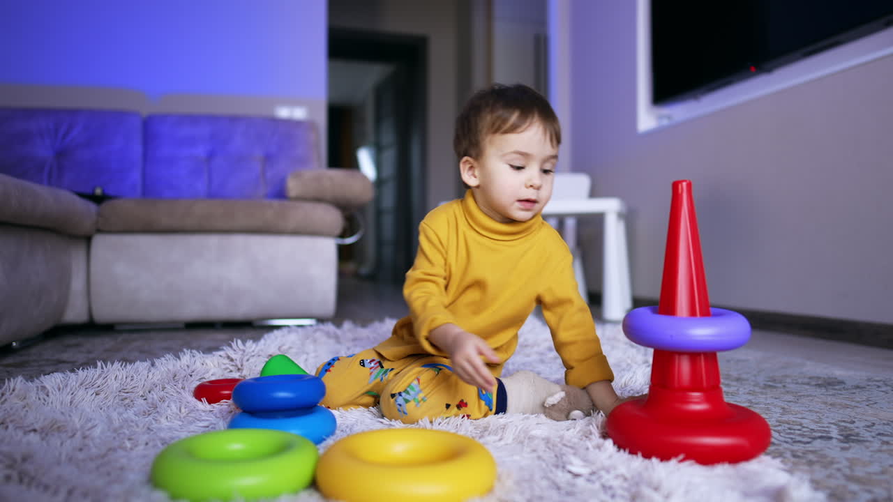 Little Caucasian toddler sitting on the soft plaid playing with a toy. Baby boy collecting a pyramid.