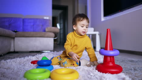 little caucasian toddler sitting on the soft plaid playing with a toy. baby boy collecting a pyramid.
