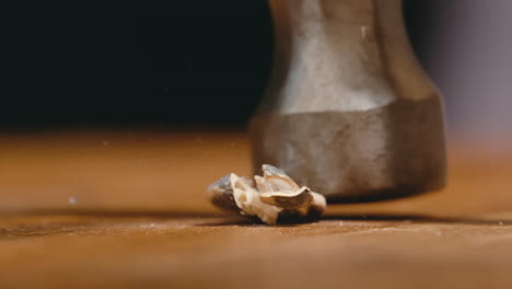 close up of hammer coming down on single sunflower seed, cracking it open in slow motion