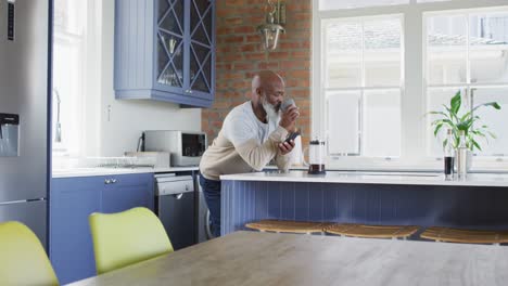 Hombre-Afroamericano-Senior-Tomando-Café-Y-Usando-Un-Teléfono-Inteligente-En-Casa