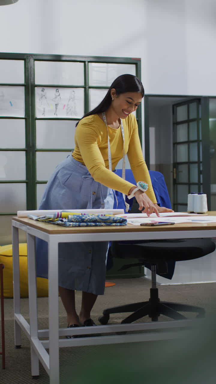 video vertical de una diseñadora biracial de pie en un escritorio en la oficina