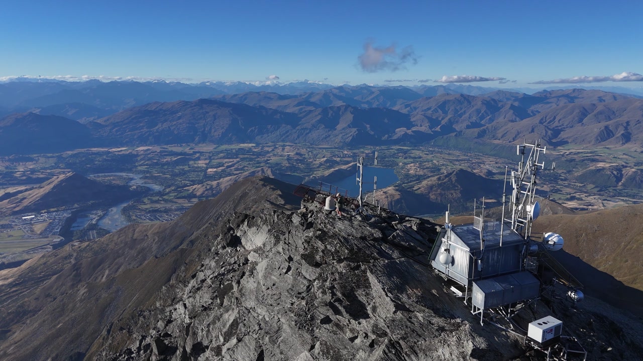 Flyover telecom tower on jagged rocky mountain summit on sunny day