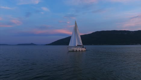 Sailboat-cruises-across-glassy-waters-of-Lake-Maggiore-at-dusk,-Aerial-drone-shot