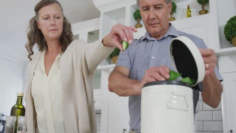 pareja caucásica de alto nivel en la cocina preparando comida, compostando restos de verduras