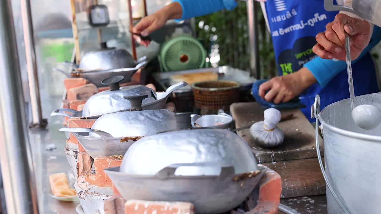 Vendors prepare traditional Thai coconut snacks using metal molds on a street in Phuket, Thailand. Bright, natural lighting enhances the scene