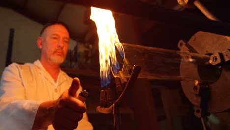 vista de ángulo bajo de un trabajador masculino maduro iluminando vidrio soplando antorcha en una fábrica de vidrio 4k