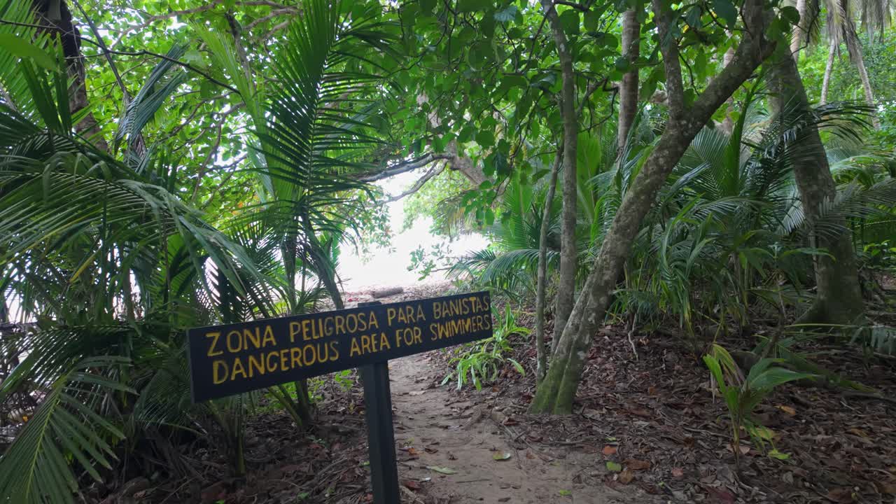 Dangerous area for swimmers warning sign at the walkway surrounded by lush green tropical forest in the Cahuita National Park, Costa Rica